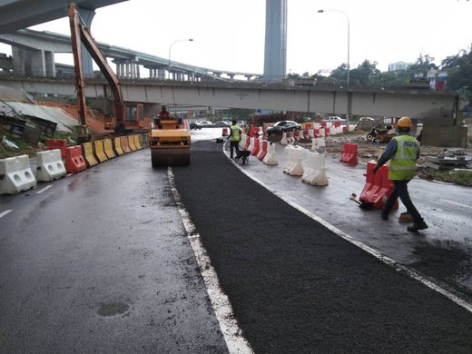Laying and compacting a new wearing course beside live traffic — Muhibah Konsortium Holdings civil works